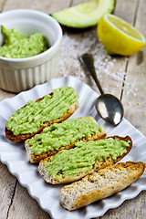 Image showing Toasts with avocado guacamole on white plate closeup on rustic w