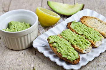 Image showing Crostini with avocado guacamole on white plate closeup on rustic