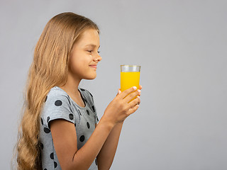 Image showing A girl holds a glass of juice in her hands with two hands, profile view