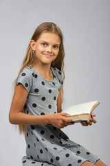 Image showing A girl of ten years distracted from reading a book and happily looked into the frame