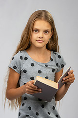 Image showing Beautiful ten year old girl reads a book and looks into the frame