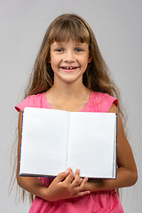 Image showing The girl cheerfully shows the opened empty book in her hands