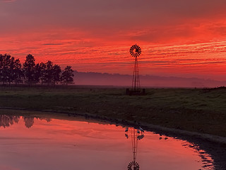 Image showing Light morning fog, windmill, pond with red sunrise sky in rural 