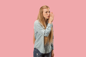 Image showing The young woman whispering a secret behind her hand over pink background