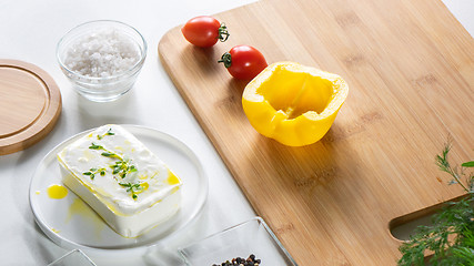 Image showing Fresh cheese, peppers and tomatoes on a wooden board on a white kitchen table. Ingredients for salad.