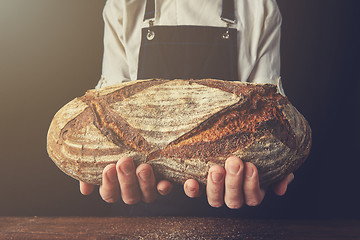 Image showing Baker\'s hands hold an oval bread.