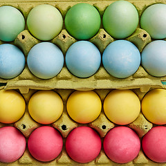 Image showing Different colored painted Easter eggs in yellow cardboard boxes. Creative Easter pattern as layout. Flat lay