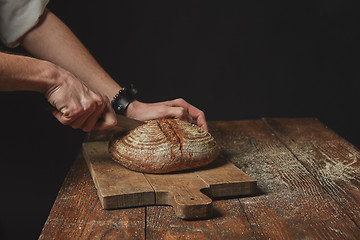 Image showing on wooden board man slicing fresh organic bread