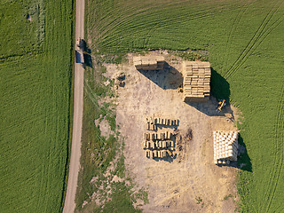 Image showing Aerial view from drone into area with stacks of straw after harvesting the grain and dirty road with tractor on it.