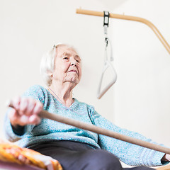 Image showing Elderly 96 years old woman exercising with a stick sitting on her bad.