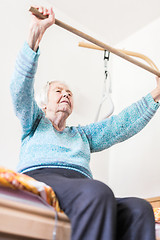 Image showing Elderly 96 years old woman exercising with a stick sitting on her bad.