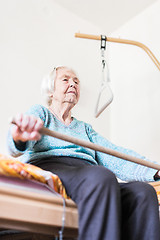 Image showing Elderly 96 years old woman exercising with a stick sitting on her bad.