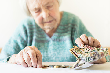 Image showing Concerned elderly woman sitting at the table counting money in her wallet.