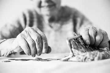 Image showing Detailed closeup photo of unrecognizable elderly womans hands counting remaining coins from pension in her wallet after paying bills. Black and white image.