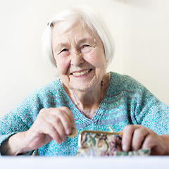 Image showing Cheerful elderly 96 years old woman sitting at table at home happy with her pension savings in her wallet after paying bills.