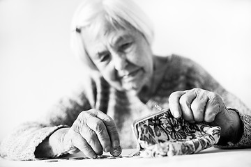 Image showing Concerned elderly woman sitting at the table counting money in her wallet. Black and white photo.