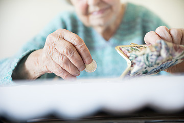 Image showing Detailed closeup photo of unrecognizable elderly womans hands counting remaining coins from pension in her wallet after paying bills.