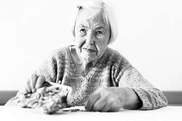 Image showing Concerned elderly woman sitting at the table counting money in her wallet. Black and white photo.