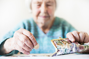 Image showing Concerned elderly woman sitting at the table counting money in her wallet.