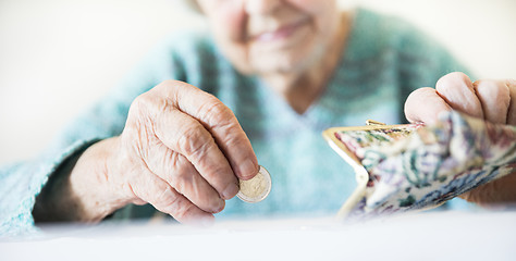 Image showing Detailed closeup photo of unrecognizable elderly womans hands counting remaining coins from pension in her wallet after paying bills.