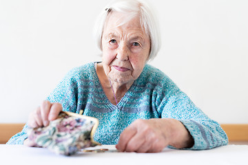 Image showing Concerned elderly woman sitting at the table counting money in her wallet.