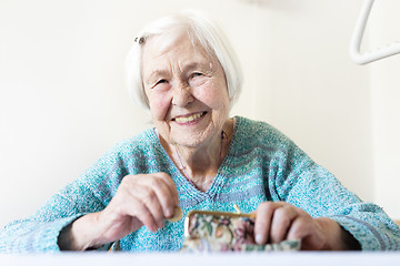 Image showing Cheerful elderly 96 years old woman sitting at table at home happy with her pension savings in her wallet after paying bills.