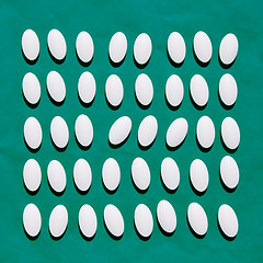 Image showing White pills on teal green background.