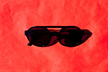 Image showing Fashionabls black sunglasses with shadow on red background. 