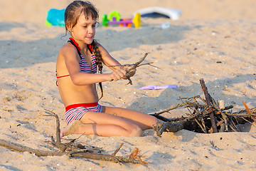 Image showing Girl breaks brushwood for a bonfire on a sandy beach