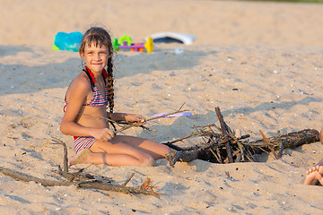 Image showing Girl breaks brushwood for a bonfire on a sandy beach and looked into the frame