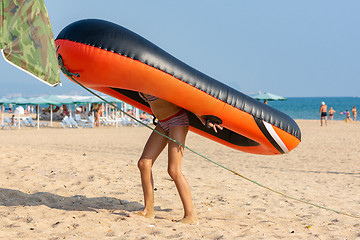 Image showing Teen girl drags on her back a large inflatable boat on a sandy beach