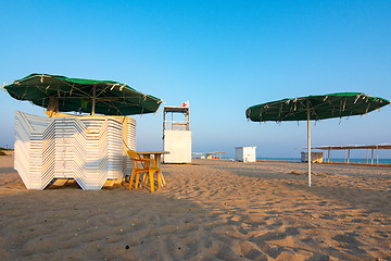 Image showing Folded sun loungers and an empty lifeguard post on a deserted sandy beach at sunset