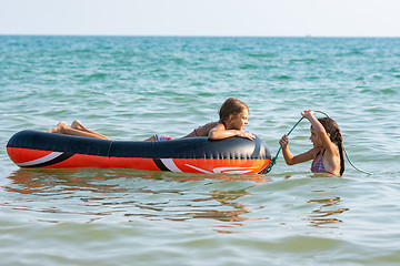 Image showing Two girls swim in the sea with an inflatable boat