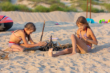 Image showing Two girls in the evening on the beach prepare a place for a fire