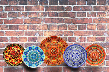 Image showing Set of decorative ceramic plates hand-painted with acrylic paints on a brick background with place for text.