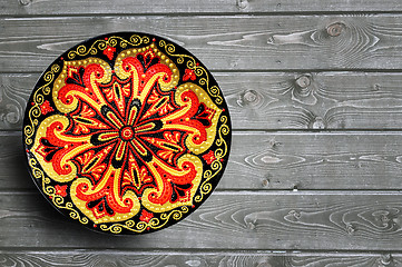 Image showing Decorative ceramic plate, hand painted with acrylic paints on a wooden background. Closeup with place for text.