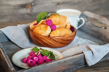 Image showing Croissants with raspberries on a wooden tray. The concept of a wholesome breakfast.