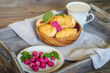 Image showing Croissants with raspberries on a wooden tray. The concept of a wholesome breakfast.