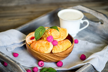 Image showing Croissants with raspberries on a wooden tray. The concept of a wholesome breakfast.