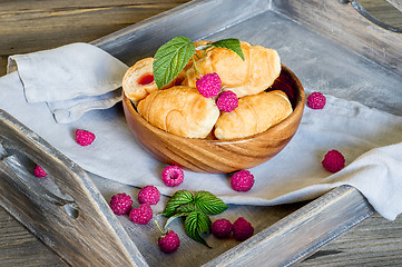 Image showing Croissants with raspberries on a wooden tray. The concept of a wholesome breakfast.