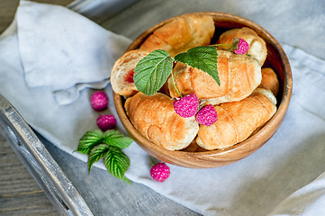 Image showing Croissants with raspberries on a wooden tray. The concept of a wholesome breakfast.