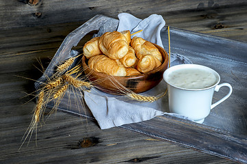 Image showing Croissants, a cup with kefir and ears of grain on a wooden tray. The concept of a wholesome breakfast.