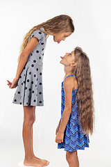 Image showing A girl stands on a chair, another girl stands nearby, show each other tongues