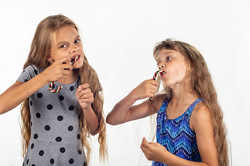 Image showing Two girls eagerly bite and suck caramel candies