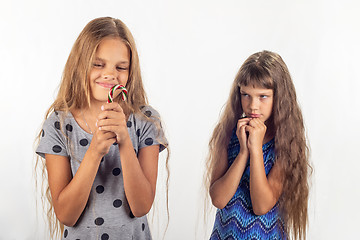 Image showing One girl has a lollipop in her hands, the other behind her looks at the girl reproachfully