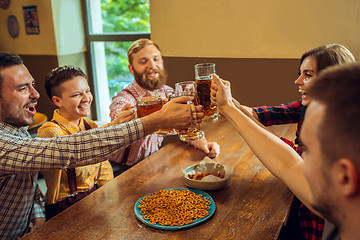 Image showing people, leisure, friendship and communication concept - happy friends drinking beer, talking and clinking glasses at bar or pub