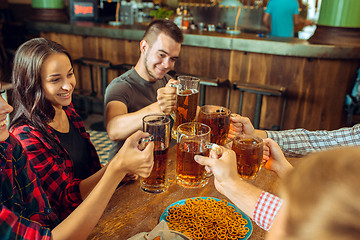 Image showing people, leisure, friendship and communication concept - happy friends drinking beer, talking and clinking glasses at bar or pub