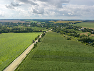 Image showing Bird\'s eye view from drone to a rural landscape with a village, dirt road and agricultural fields of planted crops at cloude background.