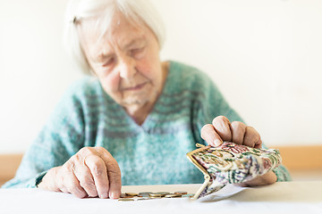 Image showing Concerned elderly woman sitting at the table counting money in her wallet.