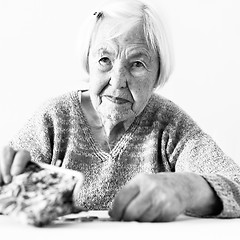 Image showing Concerned elderly woman sitting at the table counting money in her wallet. Black and white photo.